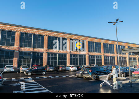 Tourcoing,FRANCE-February27,2019:Building, logo, cars in the parking lot and a woman with a shopping cart going shopping to the Lidl supermarket. Stock Photo