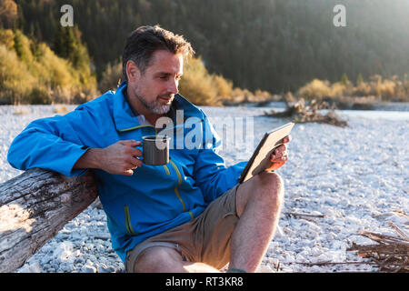 Mature man camping at riverside, using tablet Stock Photo