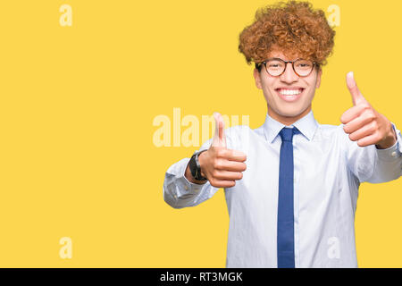 Young handsome business man with afro wearing glasses approving doing positive gesture with hand, thumbs up smiling and happy for success. Looking at  Stock Photo