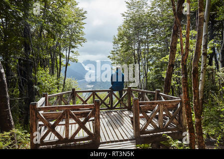 Chile, Chaiten, Parque Pumalin, man sitting on observation deck looking at glacier Stock Photo