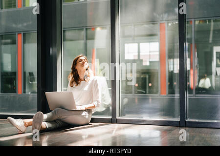 Businesswoman sitting on ground in empty office, using laptop Stock Photo
