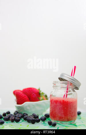 A jug with strawberry juice and a bowl full of small strawberries in the background with copy space Stock Photo