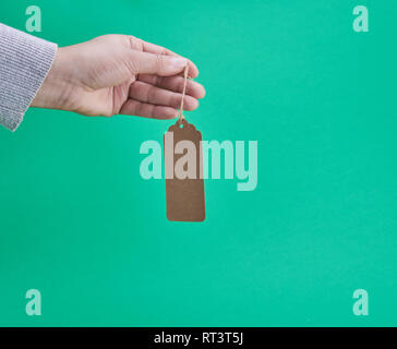 female hand holding a paper brown blank tag on a rope,green background Stock Photo