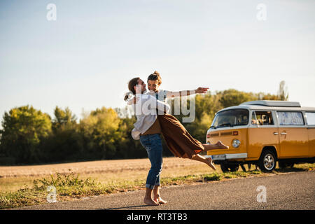 Happy couple doing a road trip with a camper, embracing on the road Stock Photo