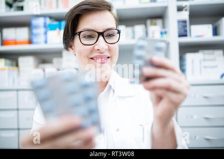 Smiling pharmacist holding tablet package in pharmacy Stock Photo
