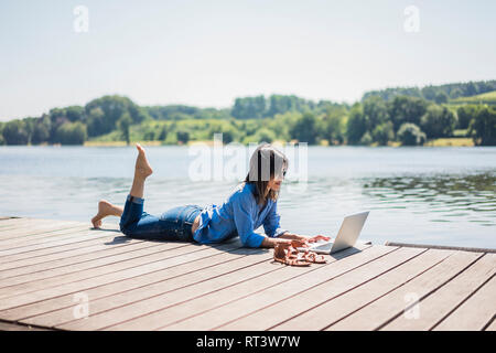 Mature woman working at a lake, using laptop on a jetty Stock Photo