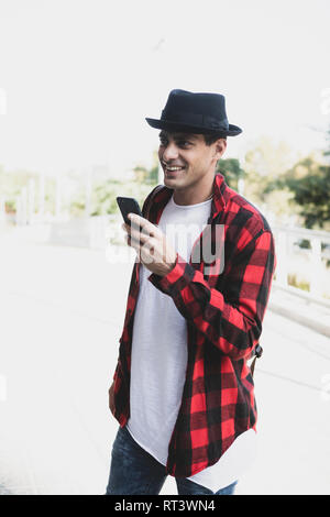Smiling young man wearing hat and holding cell phone outdoors Stock Photo