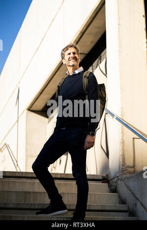 Smiling mature man with a backpack on stairs in the city Stock Photo
