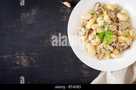 Gnocchi with a mushroom cream sauce and parsley  in bowl on a dark background. Top view Stock Photo