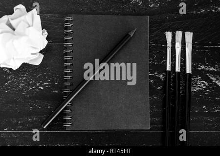 black notepad on dark desk with brushes and scrunched paper balls, concept of creativity and inspiration Stock Photo