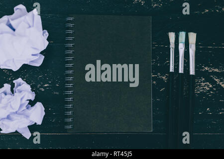 black notepad on dark desk with brushes and scrunched paper balls, concept of creativity and inspiration Stock Photo