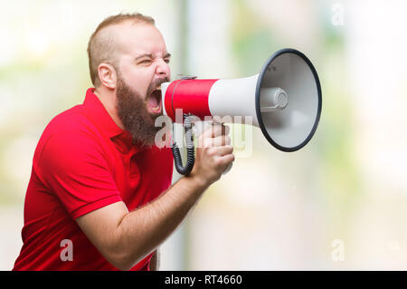 Young caucasian man shouting through megaphone over isolated background annoyed and frustrated shouting with anger, crazy and yelling with raised hand Stock Photo