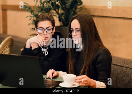 Two univercity girls watching something in the laptop while sitting at the cafeteria Stock Photo