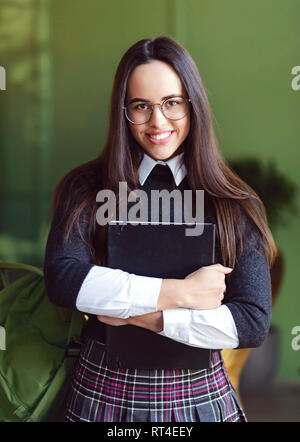 School girl in glasses standing with notepade at the cafeteria and smiling at the camera Stock Photo