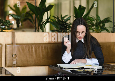 Girl wearing uniform reading something in the notebook while studying at the cafe Stock Photo