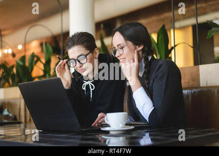 Cheerful female student girls smiling and using laptop in modern cafe Stock Photo