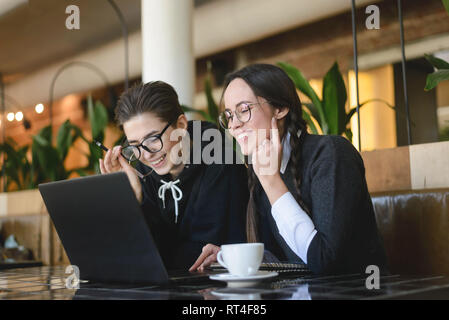 Two cheerful classmates overjoyed with great news cooperating on coursework project together in cafe Stock Photo