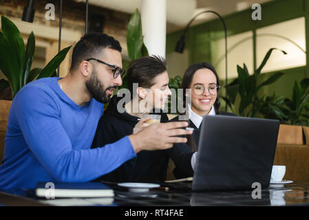 Group of friends chatting and using laptop in cafe in university talking and laughing together Stock Photo