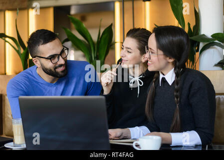 Group of joyful positive students talking, enjoying and using laptop in cafe Stock Photo