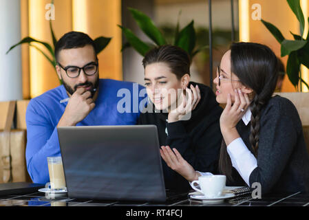 Happy smiling diverse friends doing homework and using laptop together in cafe Stock Photo