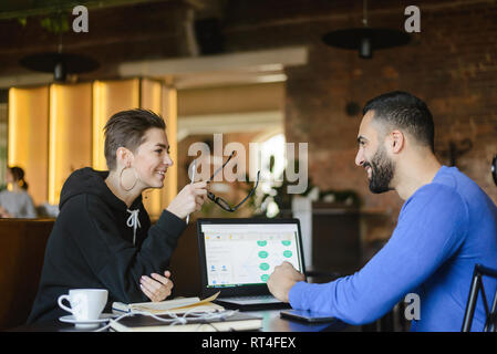 Positive male and female students cooperating using laptop computer for a learning sitting at the cafe Stock Photo