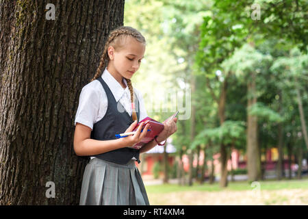 schoolgirl teenager reading a book in a park near a tree. teaches homework Stock Photo