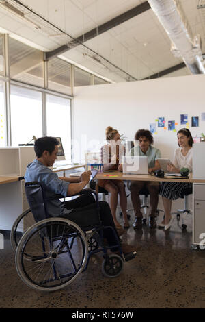 Disabled male executive using digital tablet while coworkers working in the background Stock Photo