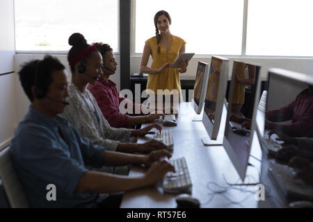 Female executive using digital tablet while coworkers talking on headset Stock Photo