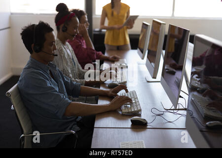 Executives working on personal computer while talking on headset in office Stock Photo