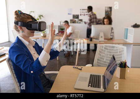 Businesswoman using virtual reality headset at desk Stock Photo