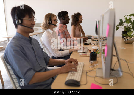 Executives working on personal computer while talking on headset in office Stock Photo