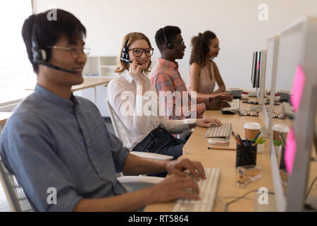 Executives working on personal computer while talking on headset in office Stock Photo