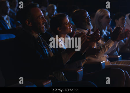 Business colleagues sitting and watching presentation with audience and clapping hands Stock Photo