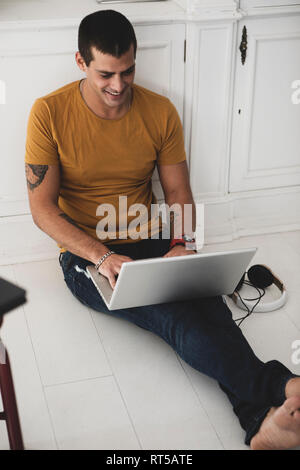 Smiling young man sitting on the floor using laptop Stock Photo