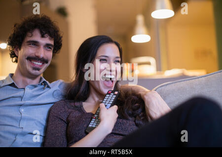 Laughing couple watching TV on sofa Stock Photo