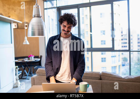 Smiling man using laptop in apartment Stock Photo