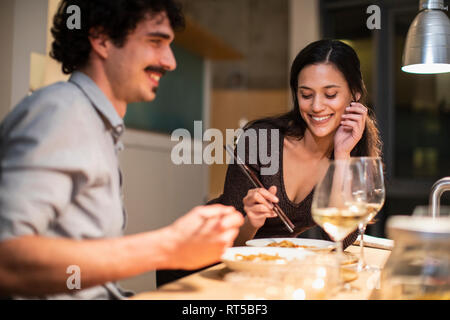 Happy couple eating dinner with chopsticks and drinking white wine Stock Photo