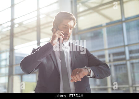 Businessman checking time while talking on mobile phone in lobby office Stock Photo