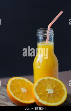 Natural orange juice together a halved orange, on a aged wooden table and black background Stock Photo