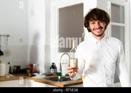 Man standing in kitchen, holding bottle of white wine Stock Photo