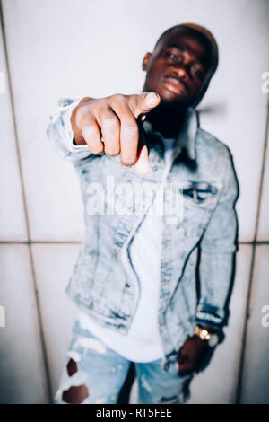 Serious young man standing at a wall pointing his finger Stock Photo