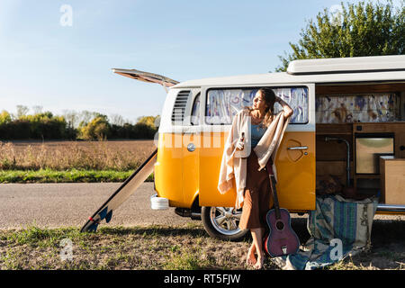 Pretty woman on a road trip with her camper, drinking beer, holding guitar Stock Photo