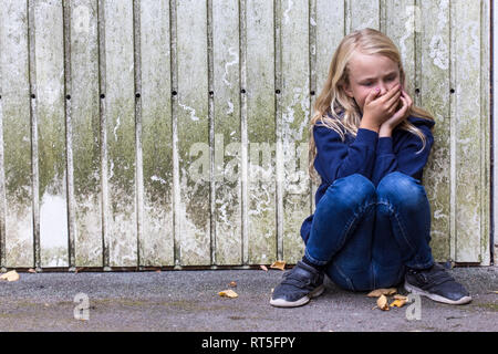 Frightened girl crouching in front of wooden wall Stock Photo