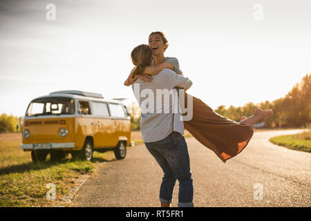 Happy couple doing a road trip with a camper, embracing on the road