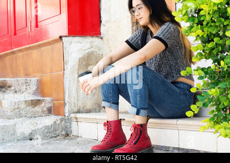 Fashionable young woman wearing  red boots sitting with coffee to go on steps Stock Photo