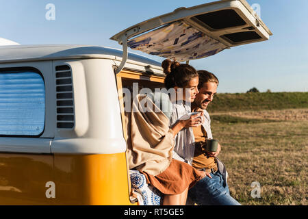 Happy couple doing a road trip with their camper, sitting on their bed, drinking coffee