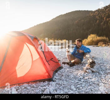 Mature man camping at riverside, using tablet Stock Photo
