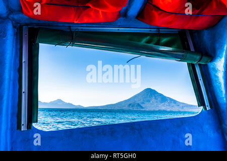 Open boat window frames view of Atitlan & Toliman volcanoes with Cerro de Oro in front on Lake Atitlan in Guatemalan highlands, Central America Stock Photo