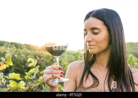 Italy, Tuscany, Siena, young woman tasting red wine in a vineyard at sunset
