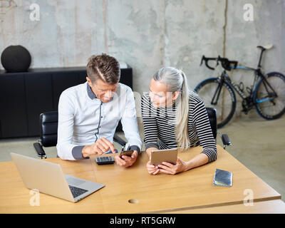 Businessman and businesswoman with cell phone and tablet in office Stock Photo
